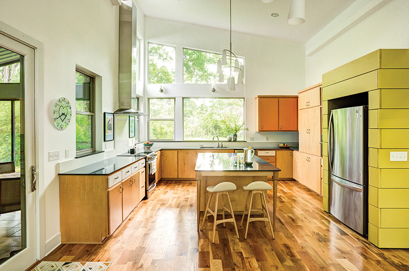 The airy kitchen, crowned by a sloped ceiling 18-feet at the high point, is a convergence of the clean lines of the Griffards’ Scandinavian-style minimalism, a warm tangerine and avocado color palette, and energy-efficient picture windows that invite the green of nature to impact the space.