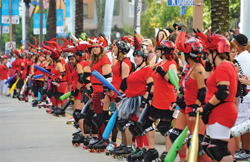 Row of people in red shirts and rollerskates, holding rubber bats