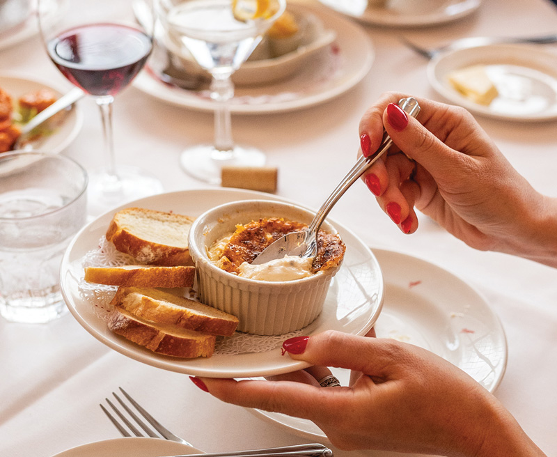 Commander's The hands of a restaurant patron, holding a small plate with her left hand; her right hand holding a spoon to dig into a ramekin.