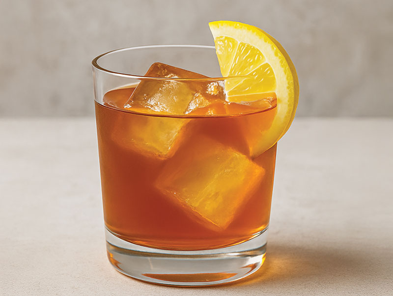 Bar Tab: Oktoberfest, Louie Louie's New Flavor & More Short alcoholic drink with two ice cubes and a lemon slice. (Black and Gold Rush cocktail)