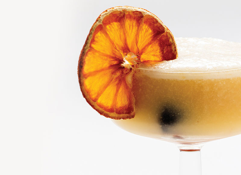 Antoine’s Hallows' Eve Sour -- a light colored drink with a dried orange and an cherry floating at the bottom of the small cocktail glass