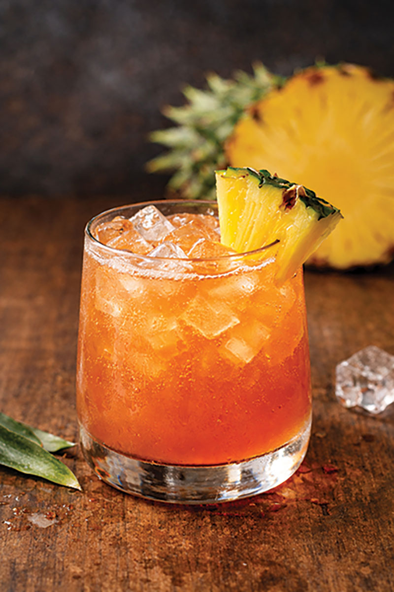 Everyone's Heard drink in a short glass (it's orange colored with a pineapple slice on the rim)