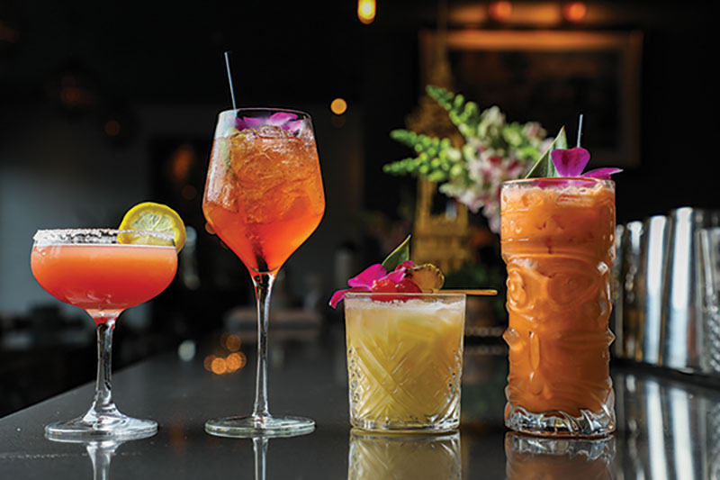 Four mixed drinks in differing colors and sizes sit on top of a bar counter.