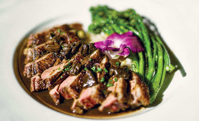 Southern Escapes Along the Gulf Coast Steak cut and spread on a white plate with asparagus and an edible purple flower